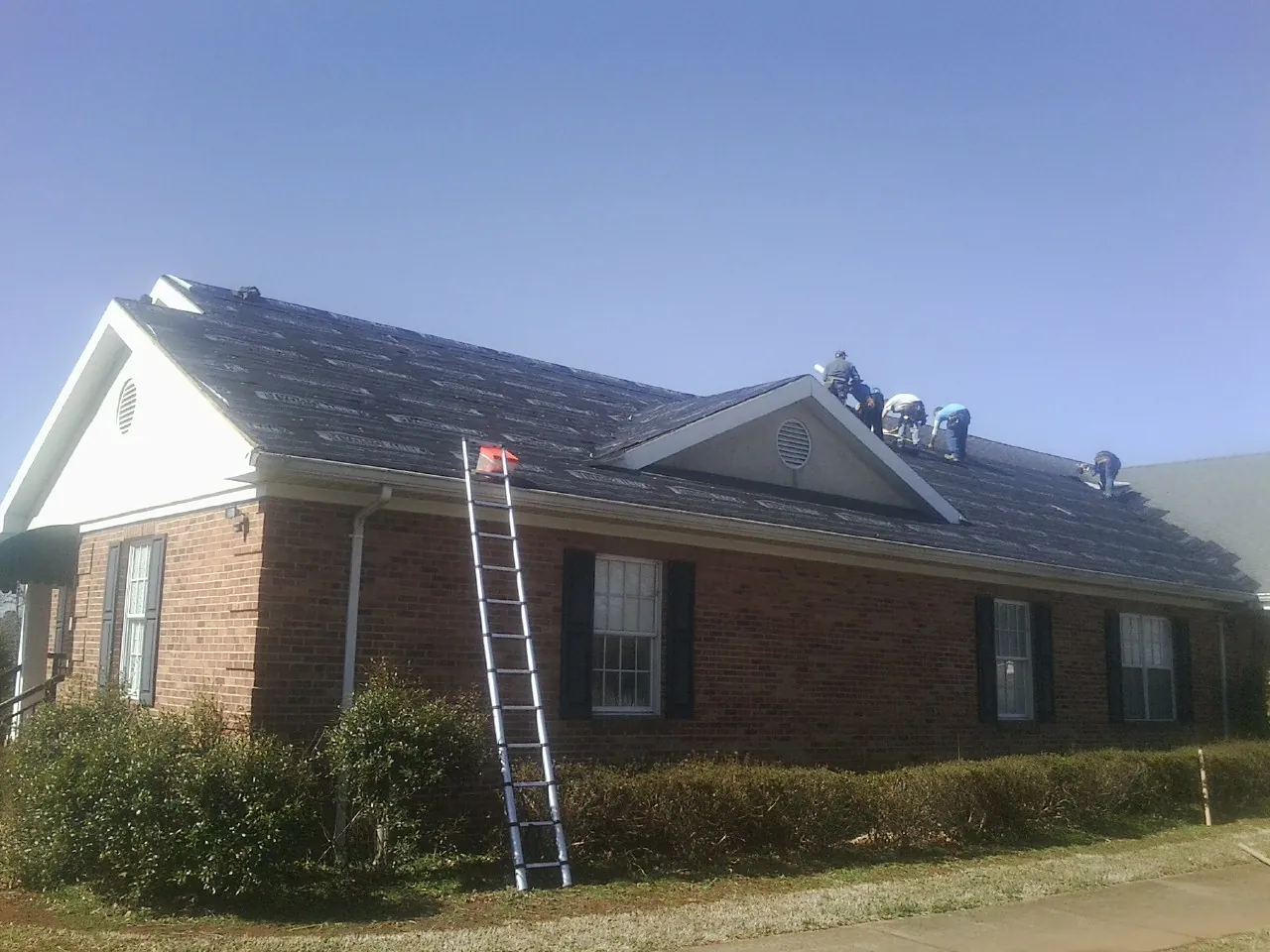 Crew tearing shingles off a brick ranch roof with a ladder set — Metal Roof Repair work by our crew in Thorn Hill