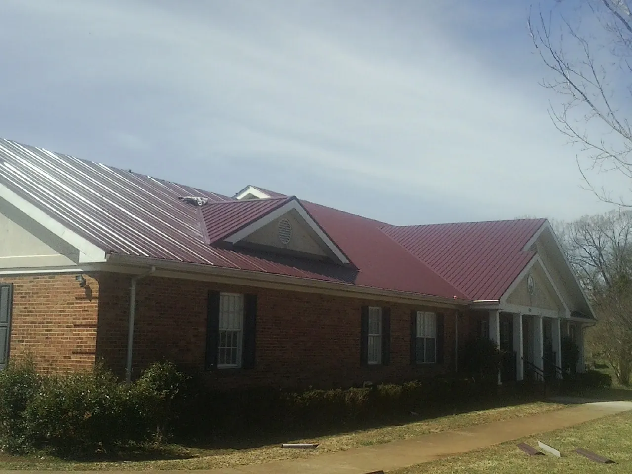 Red metal roof with gabled entries on a long brick building, from a Hail Damage Roof Repair job in Thorn Hill