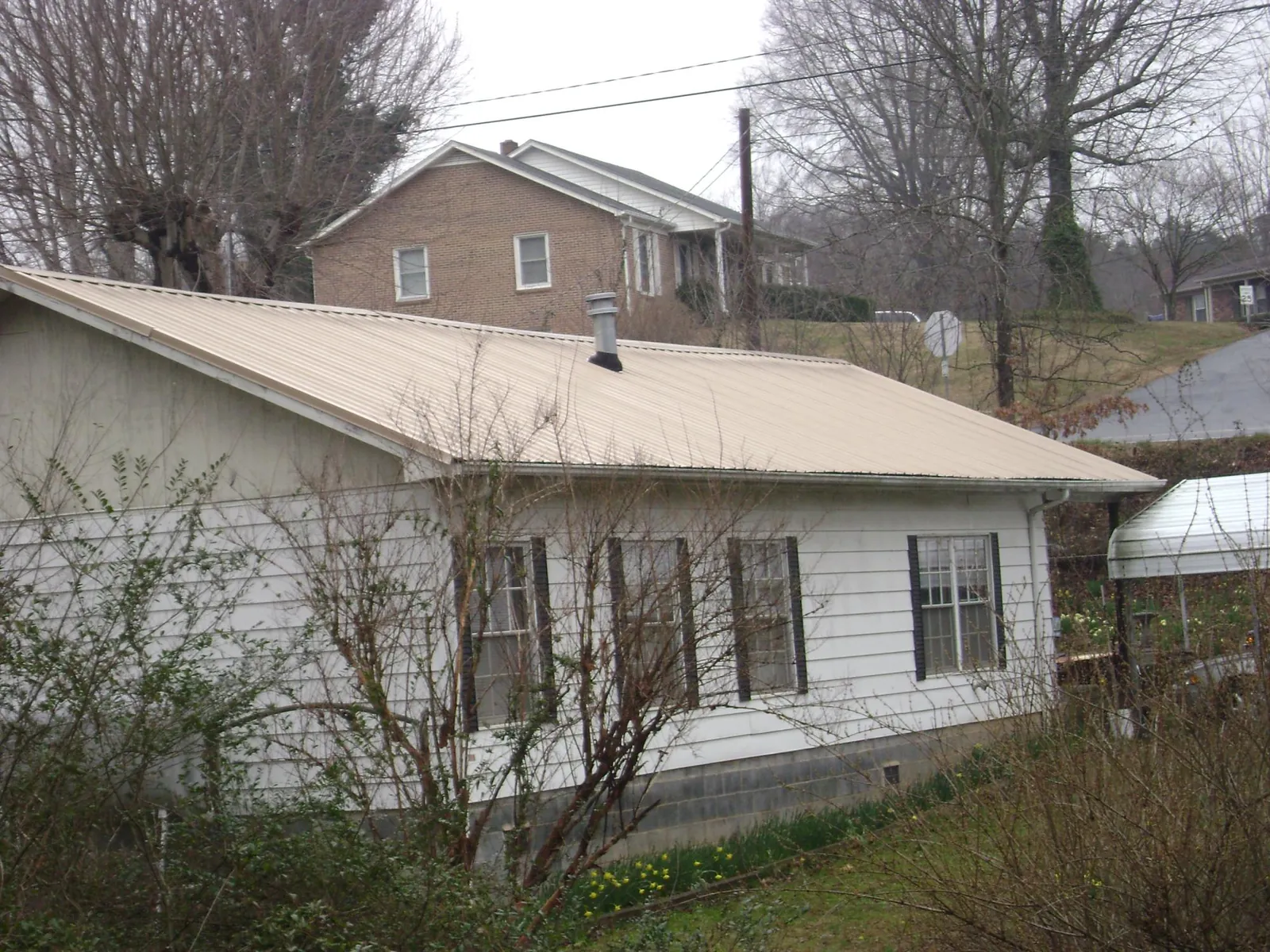 Tan metal roof on a white sided house set into a hillside — Commercial Roofing by Roofing Brothers in Thorn Hill