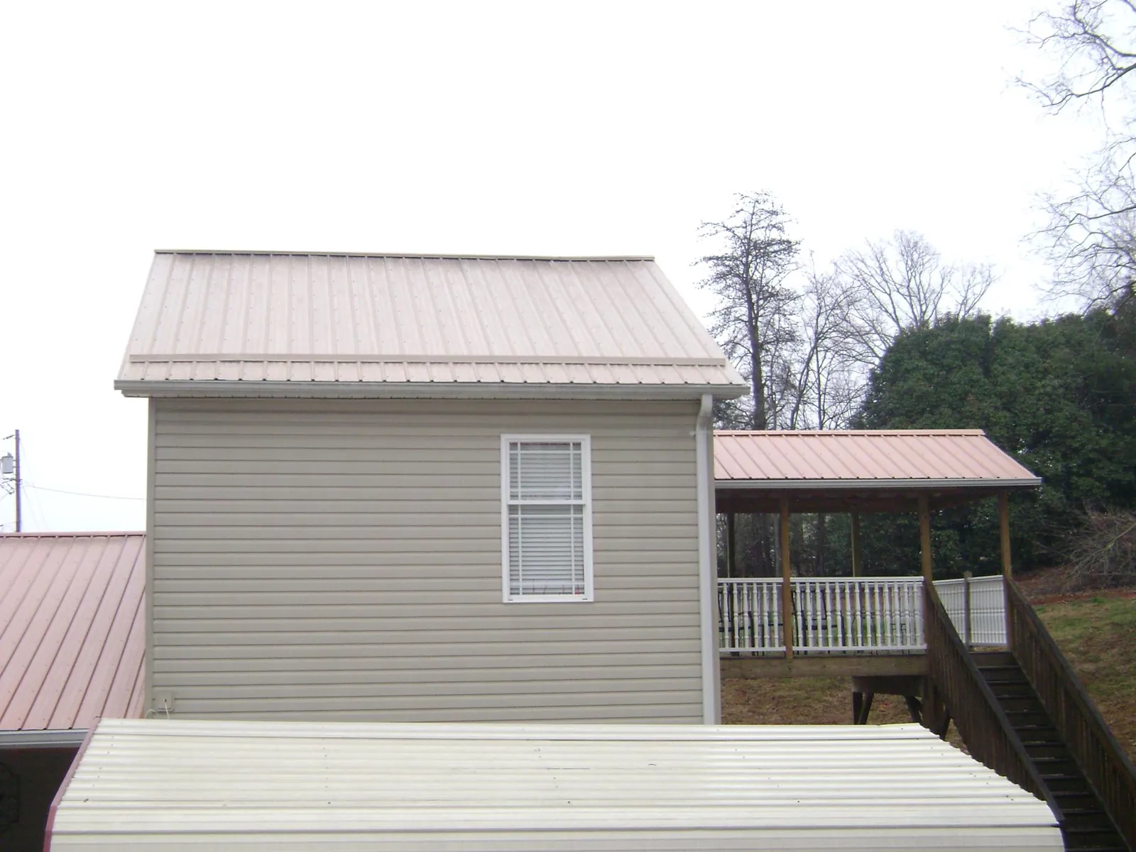 Tan metal roofs on a two story addition and attached porch, from a Roof Replacement job in Thorn Hill